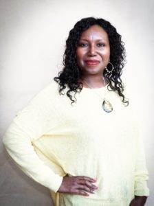 Siera London, USA Today best-selling author, is a black woman with curly black hair. She is wearing a white sweater and wearing a pendant.