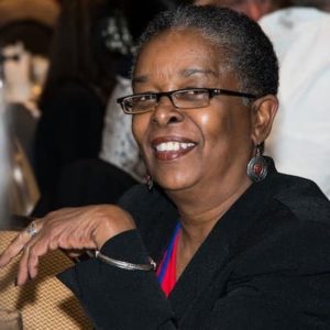 Beverly Jenkins is a black woman with short black hair, and she wears glasses.